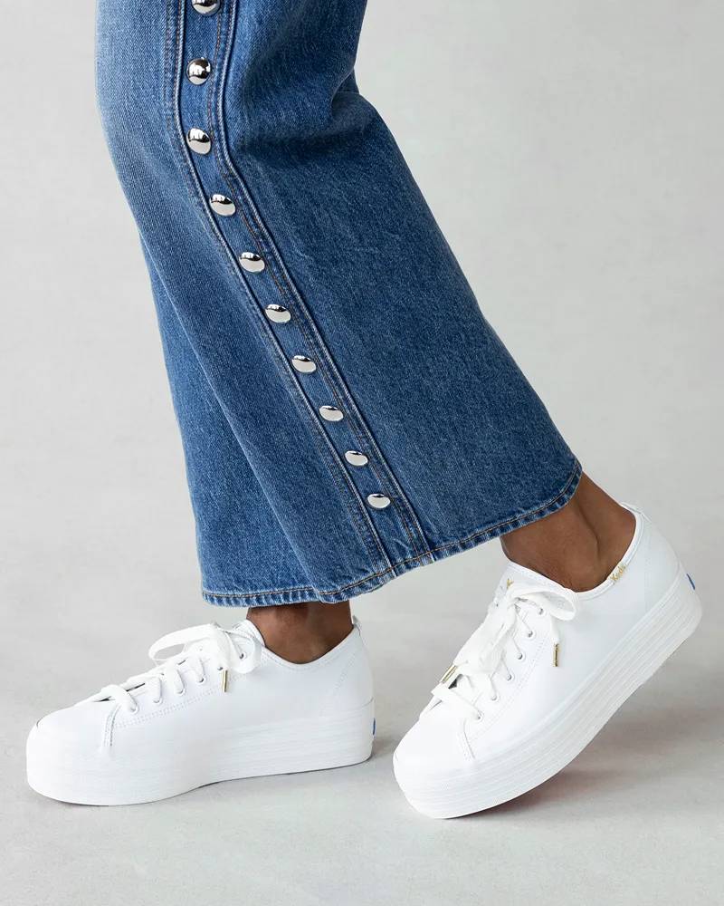 A knee-down view of a woman wearing the Triple Up Platform Leather Lace-Ups in white paired with studded wide-leg jeans.