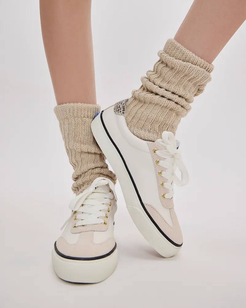 A knee-down view of a woman wearing the Jump Kick Leather and Suede T-Toe Lace-Ups in white/egret paired with beige ribbed socks.