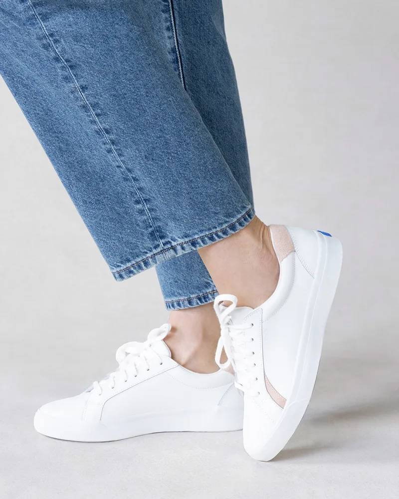 A knee-down view of a woman wearing the Pursuit Leather Lace-Ups in white/pink paired with medium-wash jeans.