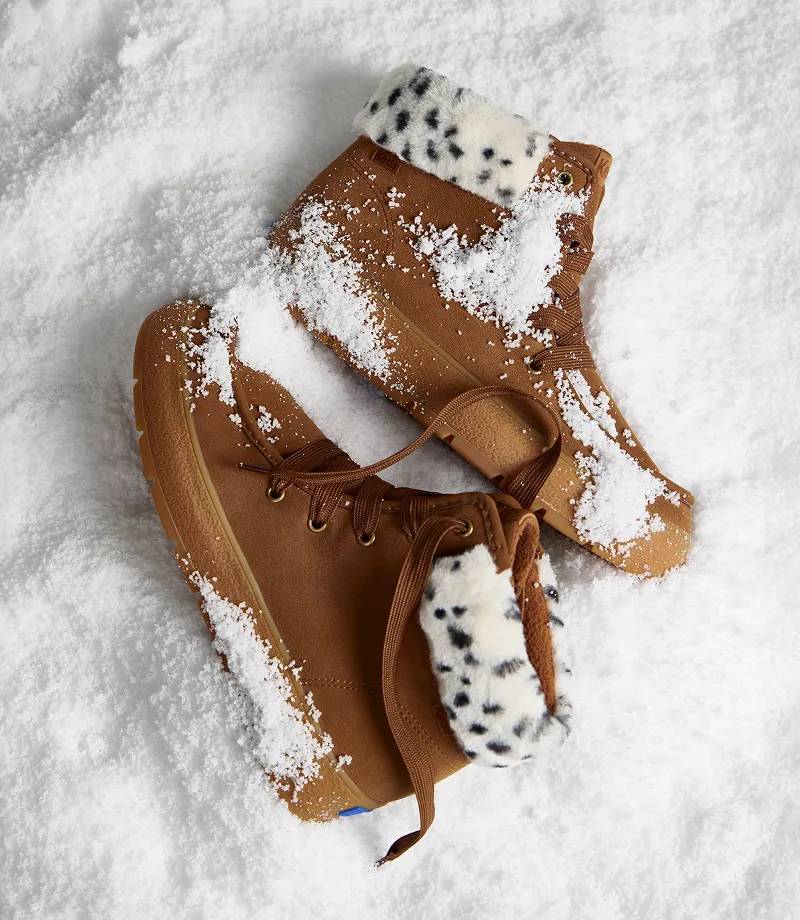 A pair of dark brown Explore Suede Booties sitting in sparkling snow.