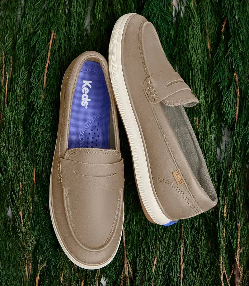 A pair of Center III Leather Loafer Sneakers in taupe shown against a background of dark green pine needles.