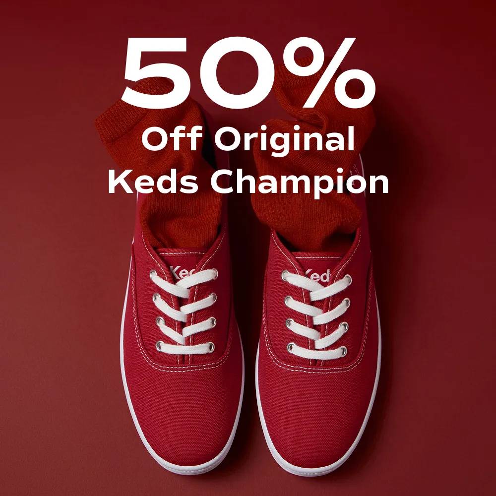 A red background with an overhead view of the Keds Champion Originals Lace-Up in red canvas with matching socks tucked in the shoe. The text says 50% Off Original Keds Champion