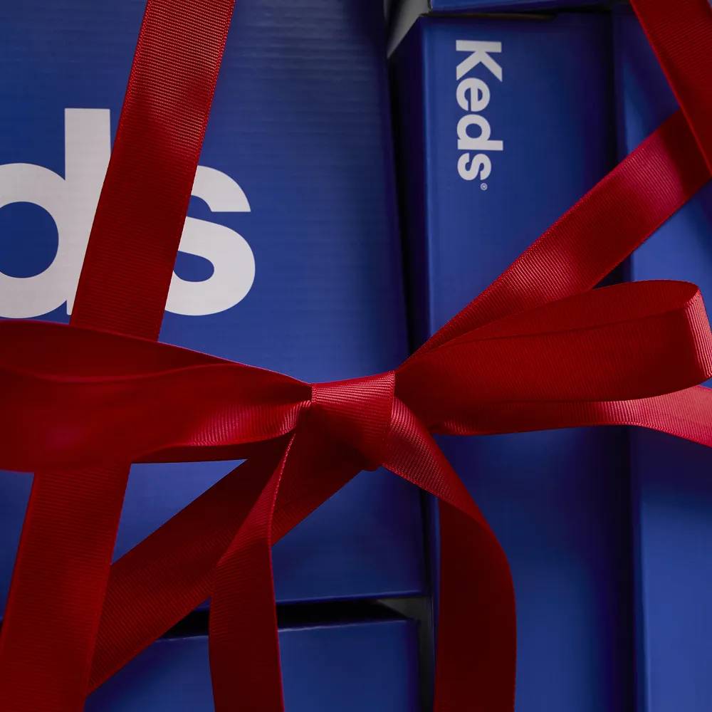 A close-up of Keds shoeboxes wrapped with a red bow.