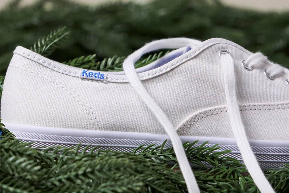 A close-up of the Keds Champion Canvas Lace-Up in white nestled in a pine wreath.