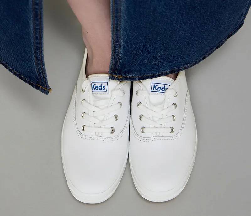 A pair of Keds Champion Leather Lace-Ups in white shown on foot paired with a dark-wash denim maxi skirt.
