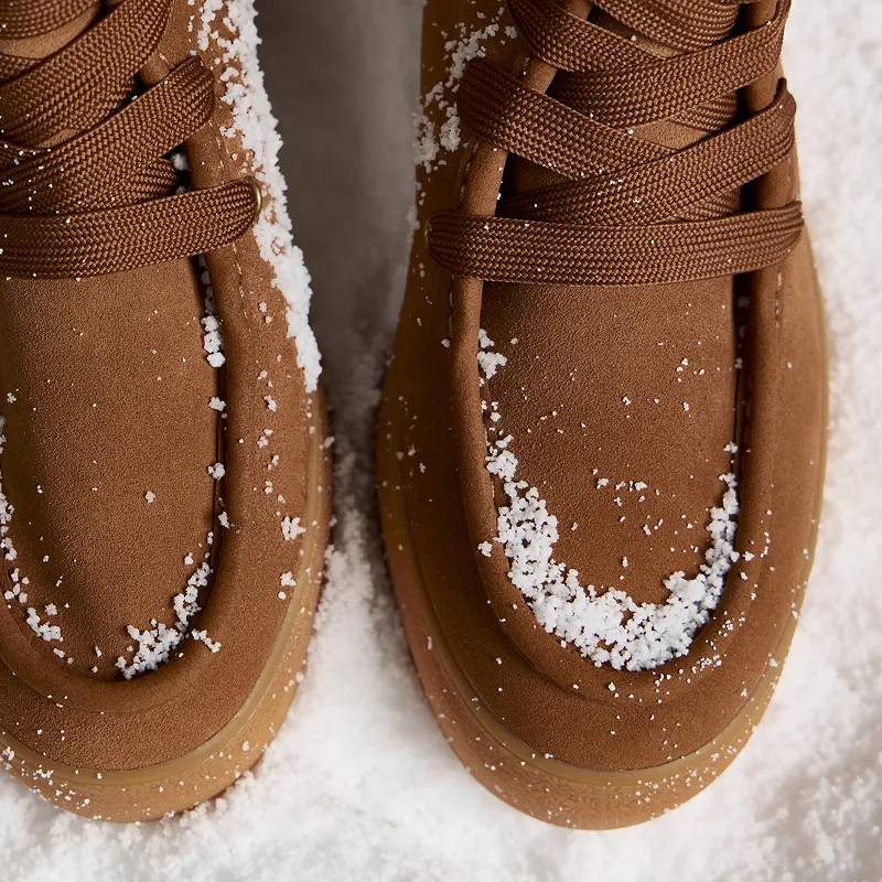 A close-up of a pair of Explore Suede Booties in dark brown sitting in snow.