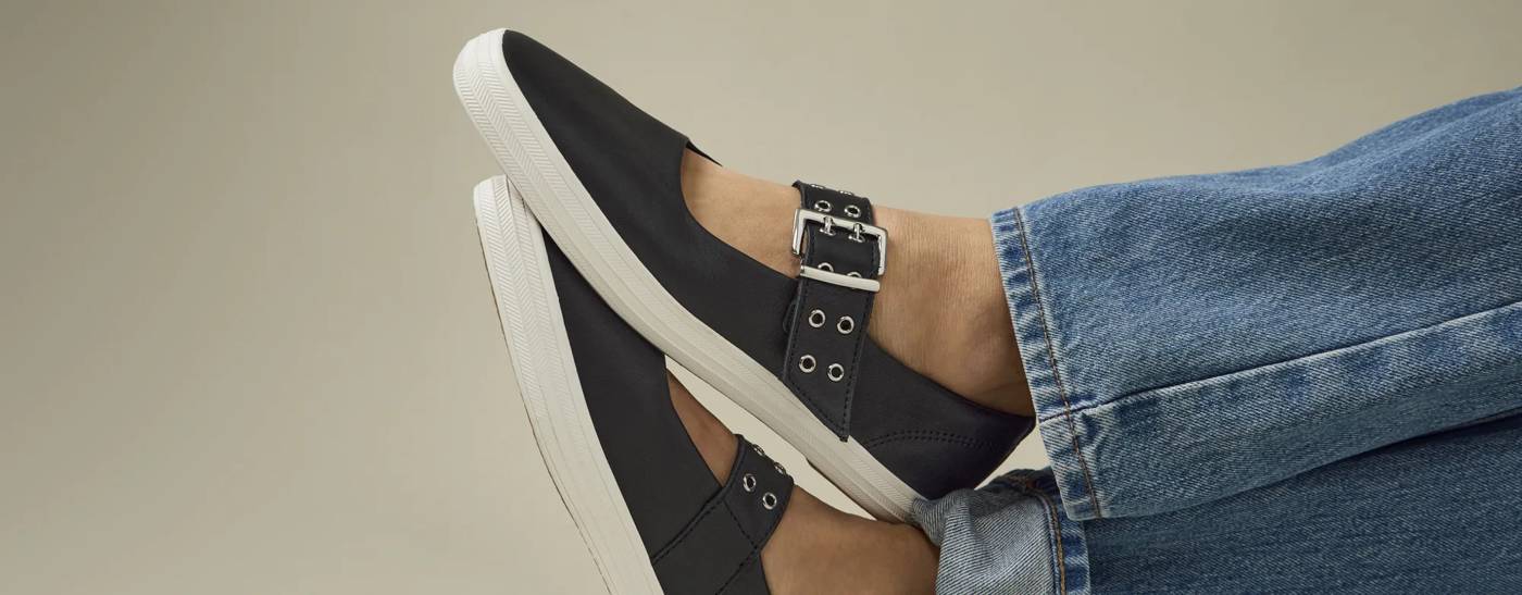 The Square Toe Mary Jane Leather Grommet Buckle in black shown on foot paired with classic jeans. Text on the image says Modern Mary Janes. Shop Now.