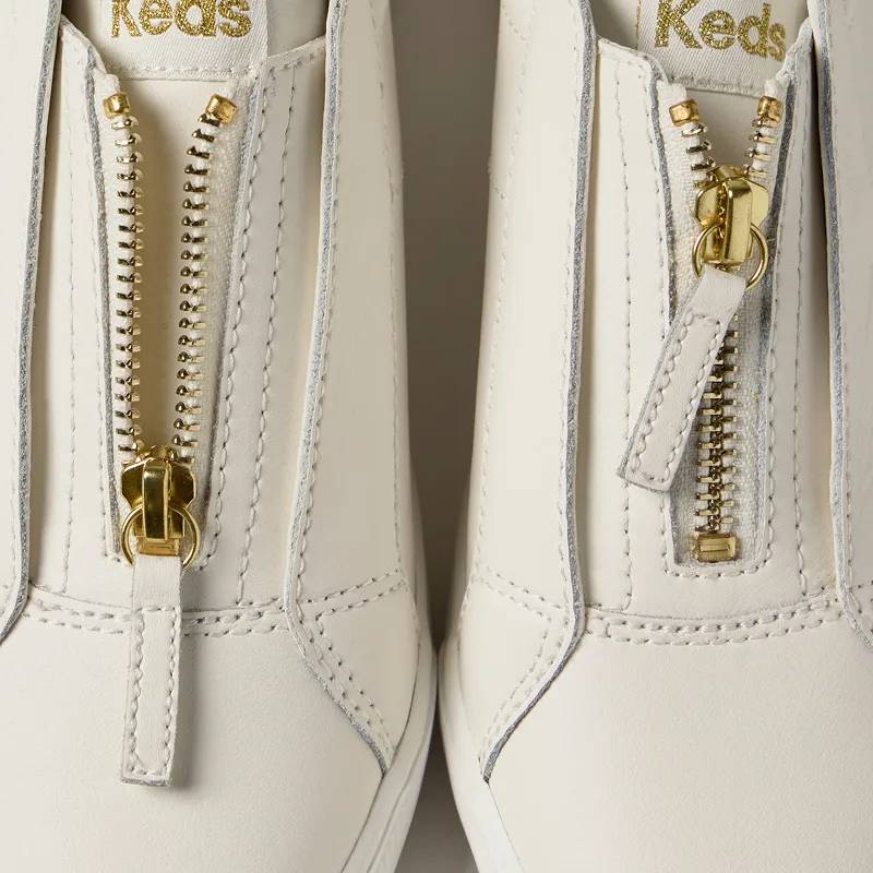 A zoomed-in top-down view of a pair of Pursuit Zip Leather Metallic Heel Slip-On in snow white/gold. Exclusive Designs. Available here and only here. Shop Online Exclusives.