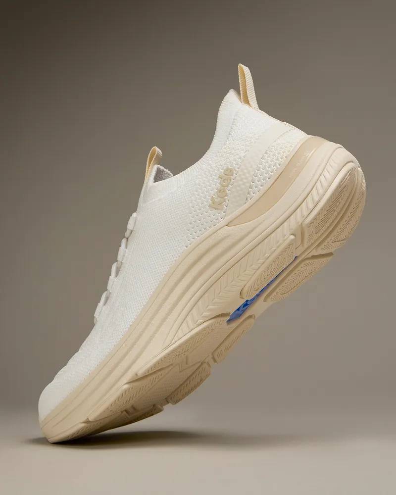 The BlissMove Knit Slip-On in parchment shown balancing on its toe showcasing the sneaker’s sculpted midsole and grooved outsole. Text under the image says Plantar Fasciitis Relief. Stabilizing support reduces strain.