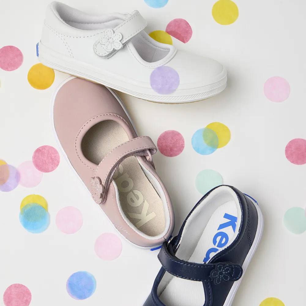A background of colorful dots featuring the Little Kids’ Ella Mary Jane in light pink, white, and navy.