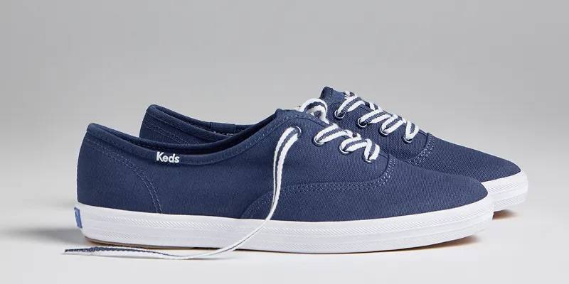 A side view of a pair of Keds Champion Canvas Lace-Ups in navy. Shop Podiatrist-Approved Keds Champion Styles.