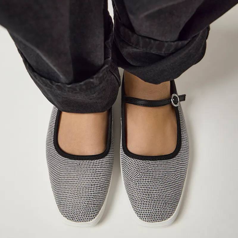 A top-down view of a pair of Square Toe Dalmata Leather Mary Jane flats in black/white shown on foot paired with black denim.
