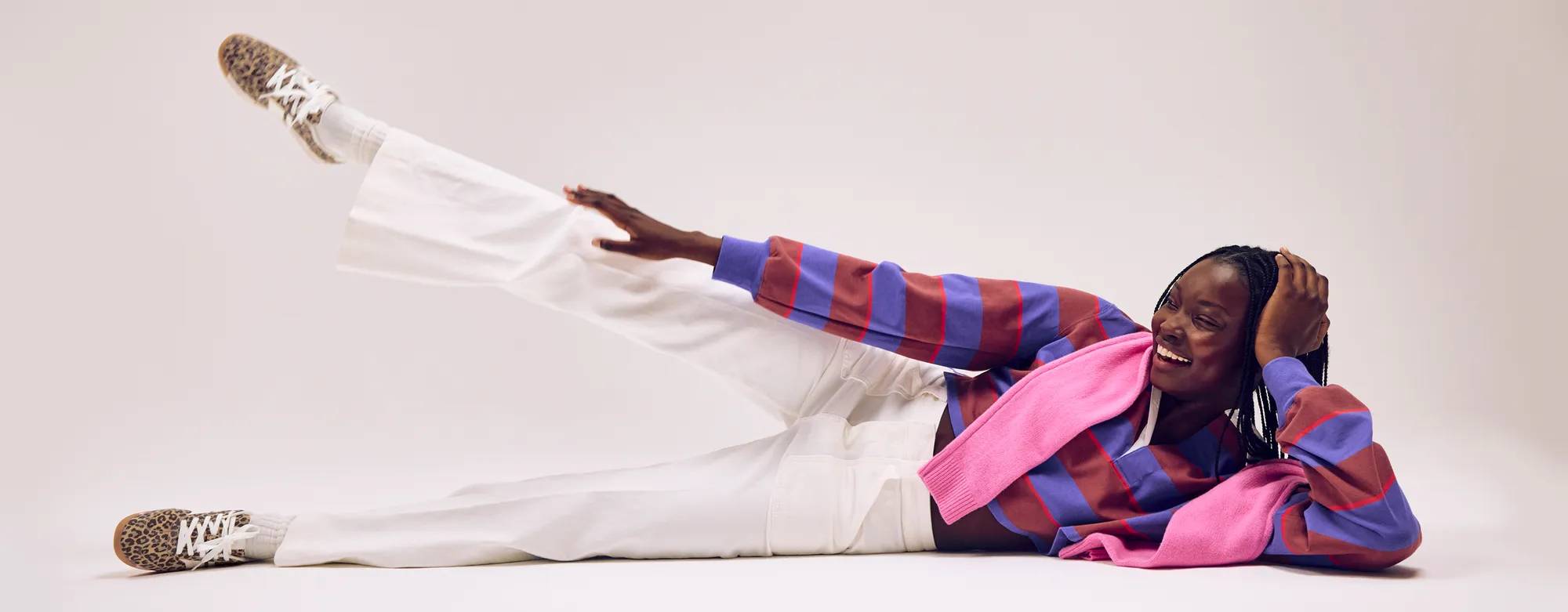 A smiling woman wearing a striped rugby top, a pink sweater around her shoulders and the Revival Suede Lace-Up in leo.