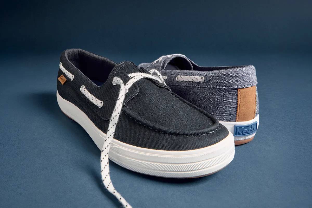 A close-up on a pair of new Center III Boat Shoes, the left shown in navy twill and the right shown in blue chambray. The angle showcases the classic moc toe construction and the dotted striped laces.
