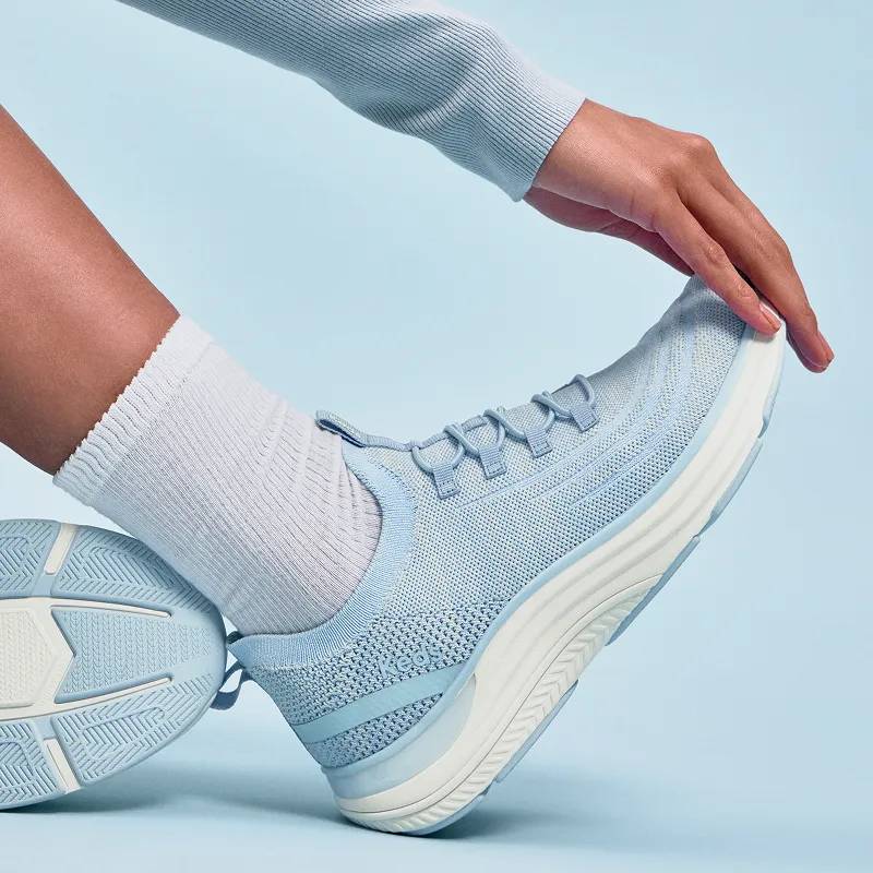 The BlissMove Knit Slip-On in light blue shown on foot paired with a matching blue sweater and white socks.