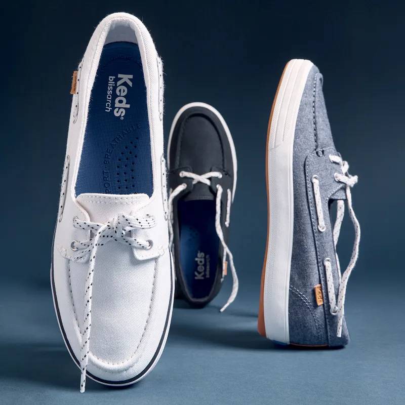 The Center III Boat Shoe in three different colorways—white twill, navy twill, and blue chambray—standing upright balanced either on the toe or heel to demonstrate the slip-ons’ lightweight design.