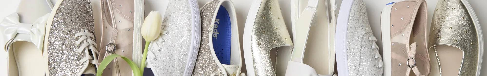 A horizontal line up of Keds occasion styles in pink, white, and gold, including an embellished Mary Jane, glitter Keds Champion Lace-Ups, and point-toe slingbacks. A white rose is tucked behind the Square Toe Mary Jane Sheer Mesh Jewels.