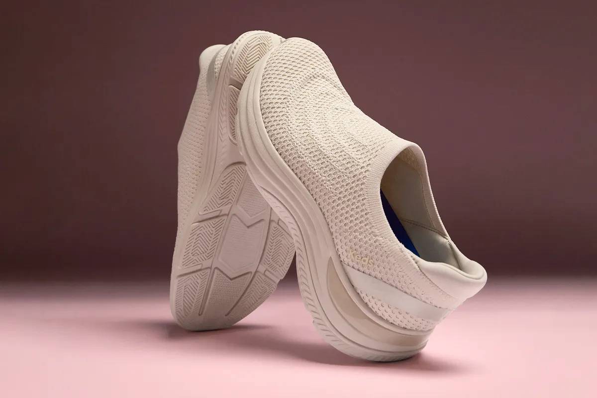 A dark to light mauve background. At the center is a pair of the BlissMove Knit Ease Slip-On in parchment positioned back-to-back with one on its heel and one on its toe.