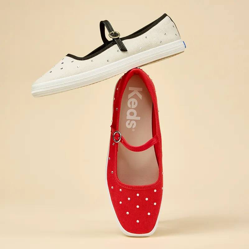 A light yellow background with the Square Toe Mary Jane Woven in red positioned on its toe and the Square Toe Mary Jane Woven in natural/black balancing on top of the red version.