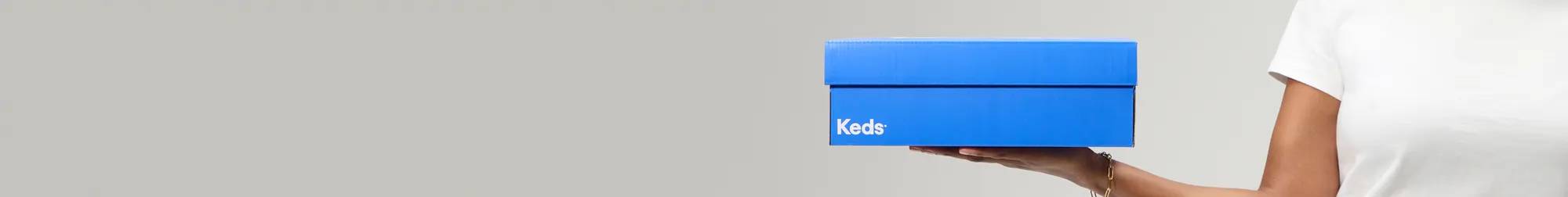 A hand holding up a bright blue Keds shoebox against a grey background. Text above says, Spring Finale Sale-on-Sale. Extra 35% Off Sale. New markdowns just added! Exclusions apply. Limited time only. Use code: EXTRA35. Shop Now.