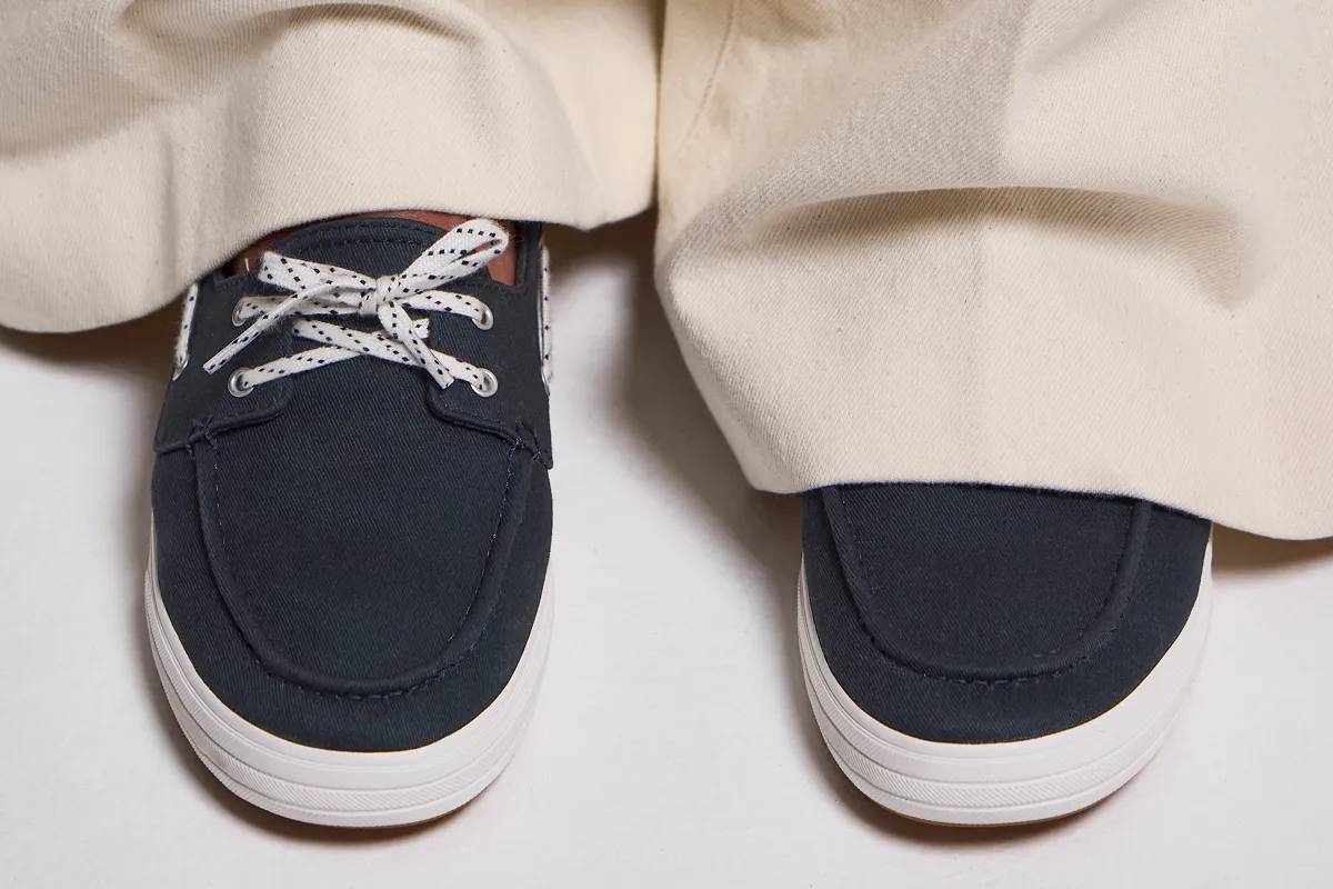 A top-down view of a pair of Center III Boat Twill Slip-Ons in navy blazer shown on foot paired with beige wide-leg pants.