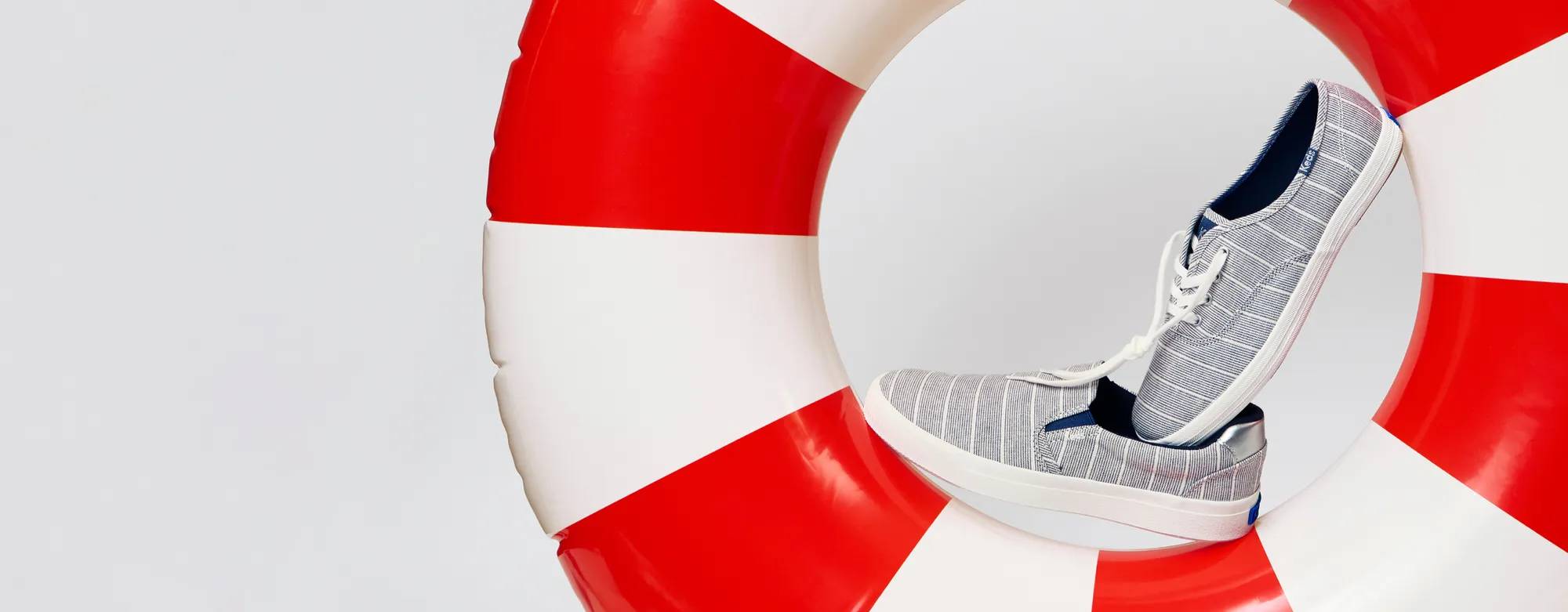 Two Keds sneakers—the Pursuit Chambray Lurex Stripe Slip-On and the Keds Champion Lurex Stripe Lace-Up both in vintage indigo—balanced on a red-and-white striped pool float. Text on the image says Pair-Up Sale. 2 for $60 including new exclusive styles! Use code: DOUBLEUP. Exclusions apply. See details. Shop now.