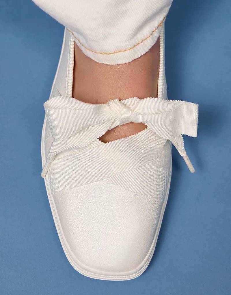 A blue background with an overhead view of the Square Toe Ballet Pearlized Leather in white paired with white jeans.