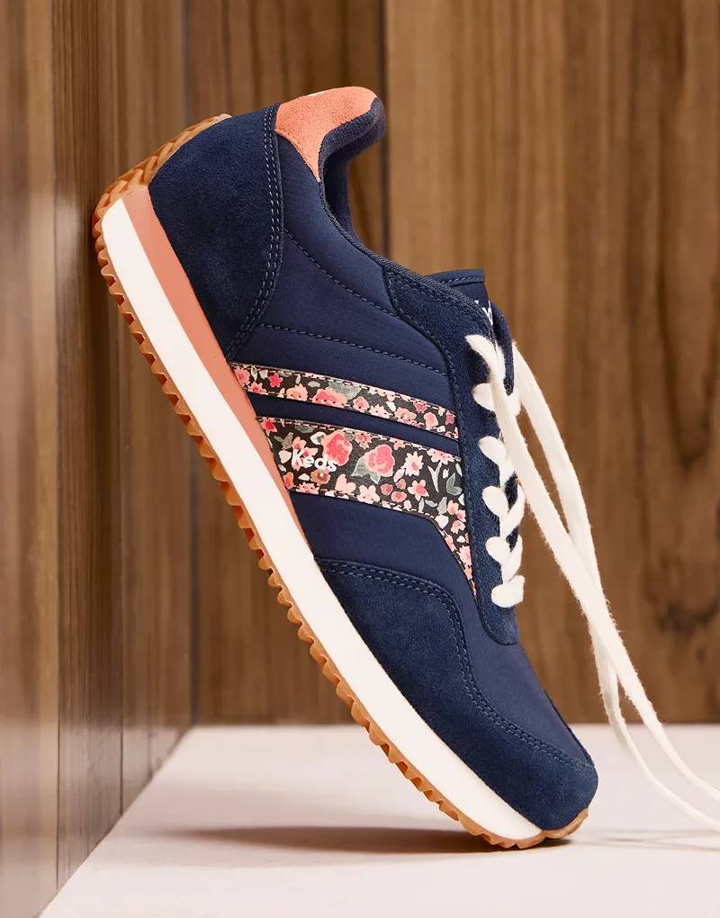 An untied Rena Nylon/Suede Ditsy Rose Lace-Up in navy blazer/clay propped against a wood-paneled wall.
