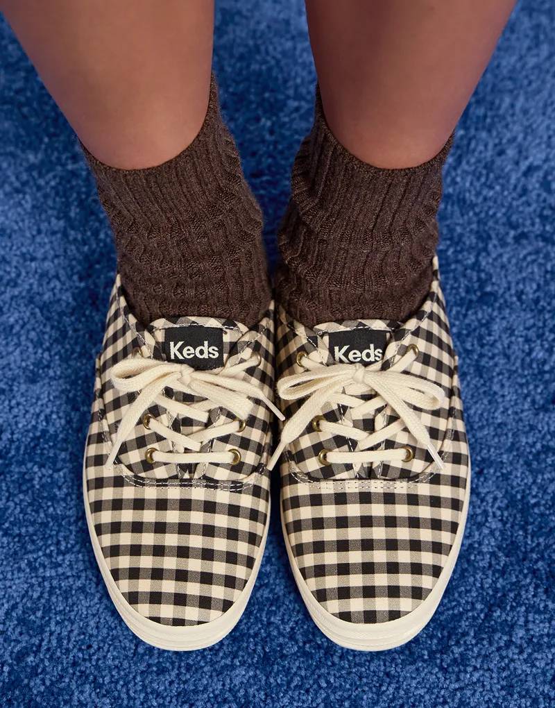An overhead view of the Keds Champion Buffalo Plaid Lace-Up in black/parchment paired with brown ribbed socks positioned on a blue carpet.
