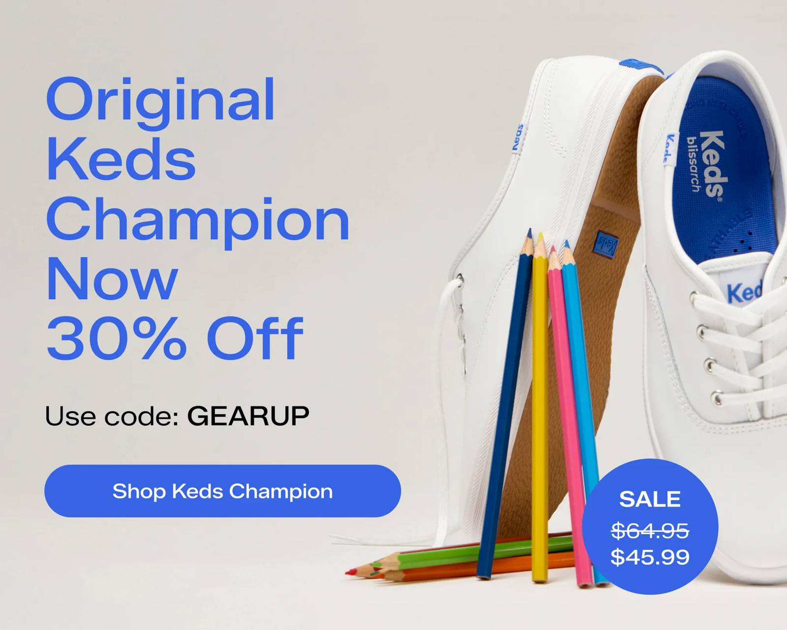 A pale grey background with a pair of the Original Keds Champion Lace-Ups in white set upright on the toes alongside an assortment of colored pencils.