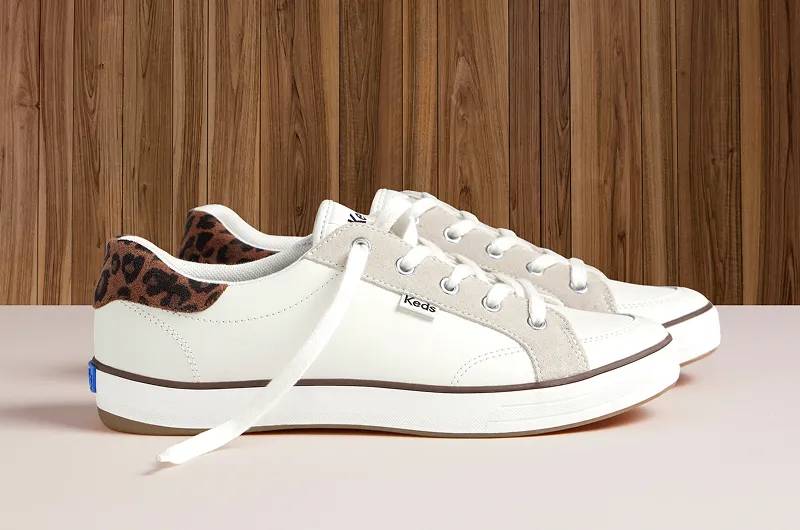 A side view of a pair of Center III Leather/Suede Lace-Ups in egret/dark brown sitting on a cream-colored floor with wood paneling in the background. Shop Leather.