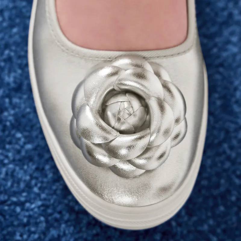 A close-up on the flower applique embellishment on the toe of the Maisie Ballet in silver metallic leather. Corresponding text says Petal to the Metal 3D florals in shiny leather.. Shop Maisie Ballet.