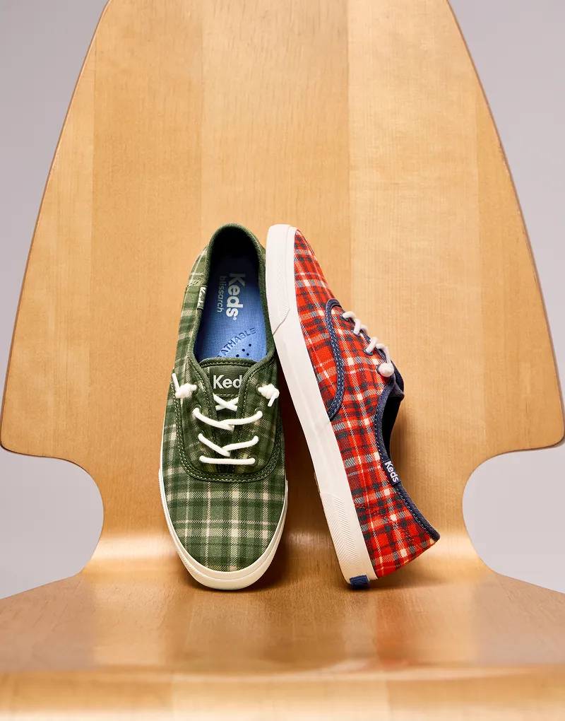 Two colors of plaid flannel Rillax Champ Slip-Ons, one in olive/oatmeal and the other in red/vintage indigo, sitting on a wooden chair.