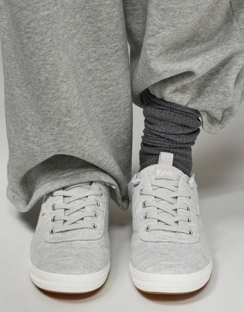 A close up, angled top-down view of a pair of Center III Slip-Ons in light grey sweatshirt jersey shown on foot paired with wide-leg heather grey sweatpants and scrunched dark grey socks.