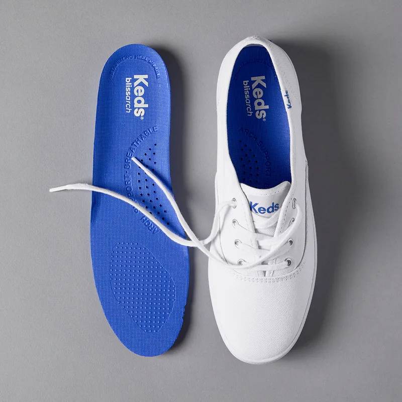 A grey background with an overhead view of the Original Keds Champion in white on the right and the BlissArch footbed on the left.