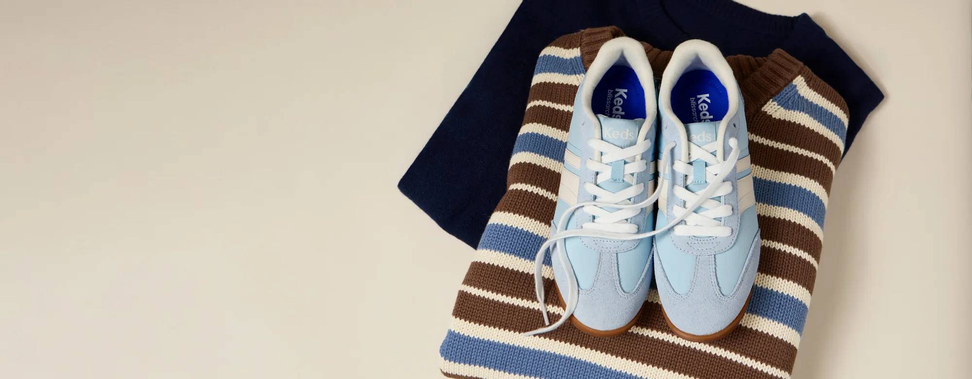 A pair of Revival Nylon/Leather/Suede Lace-Ups in light blue sitting on top of a brown, cream, and blue horizontally striped knitted sweater.