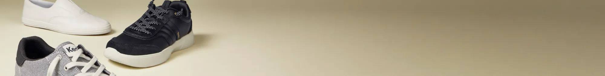 A beige background features a the Center III Two Tone Textile Lace-Up in grey/white in the foreground pointing toward the right, the BlissWalk Ubal Lace-Up in black in the middle pointing toward the left, and Keds Champion Square Toe Soft Leather Slip-On in white pointing toward the right. The text says Fall Favorites Sneaker Sale $35 Sneakers. Select styles only. See details. Use code: SNEAKS35 Shop Now