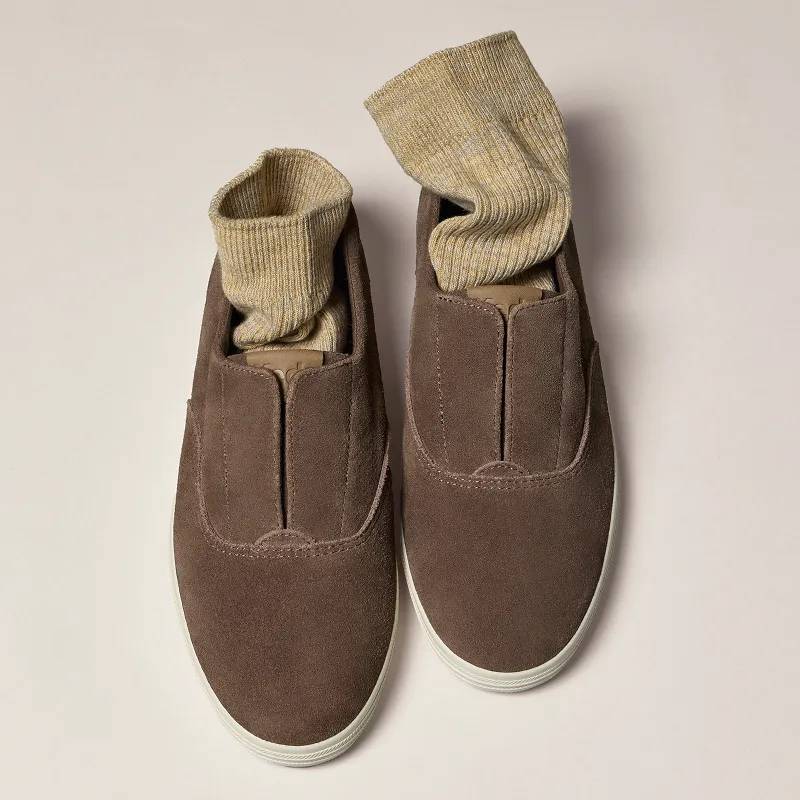 A grey background with an overhead view of the Keds Champion Round Toe Suede Slip-On in cocoa brown with a pair of tan socks tucked inside.