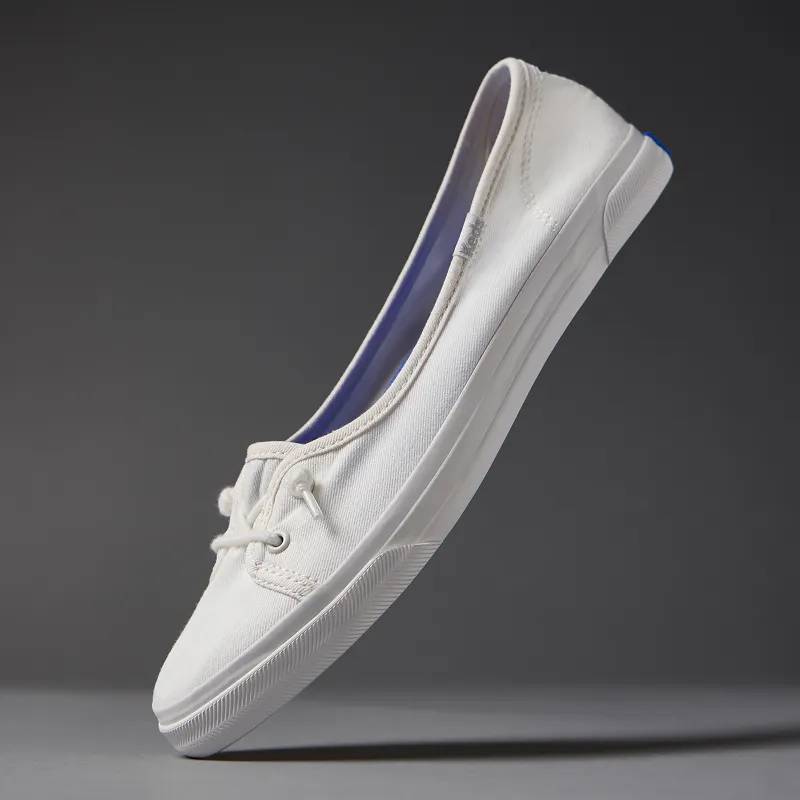 A grey background with a floating Rillax Champ Mini Washed Twill Slip-On in snow white.