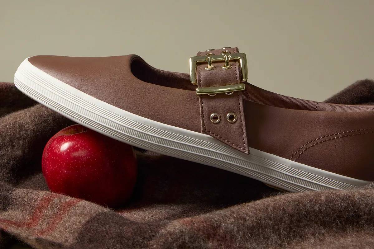 The Square Toe Mary Jane Leather Grommet Buckle in brown set on brown plaid wool blanket.