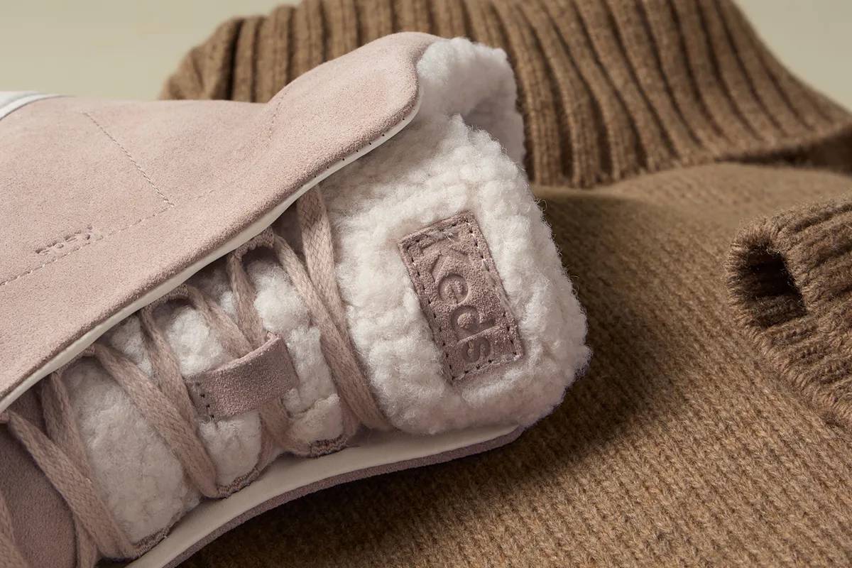 The Remi Mid Zip in light beige suede resting on a brown turtleneck sweater.