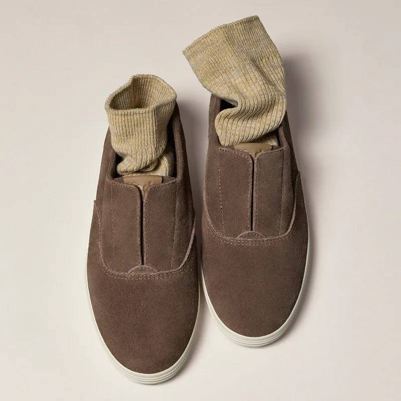 A pair of the Keds Champion Round Toe Suede Slip-On in cocoa brown with oatmeal-colored socks tucked in.