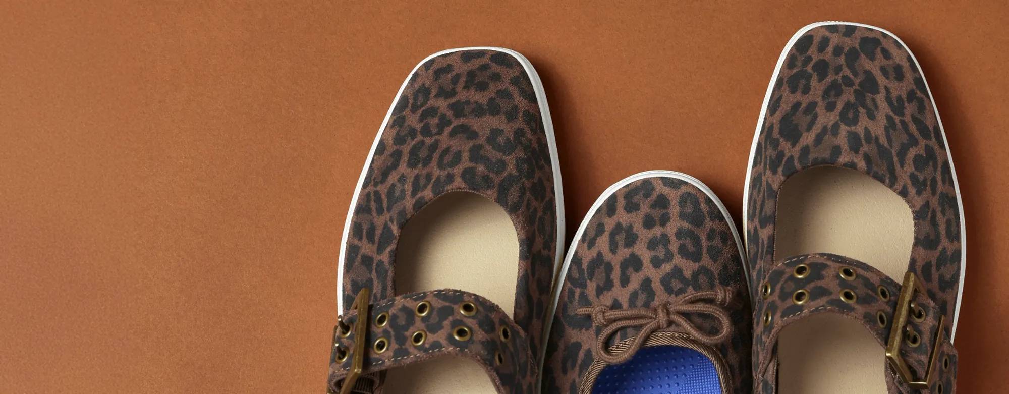 A brown background with the Maisie Ballet Leopard Suede in dark brown flanked by the Square Toe Mary Jane Grommet Leopard Suede in dark brown on each side.