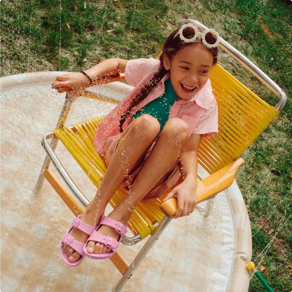 Girl getting splashed with water while wearing pink Birkenstock sandals