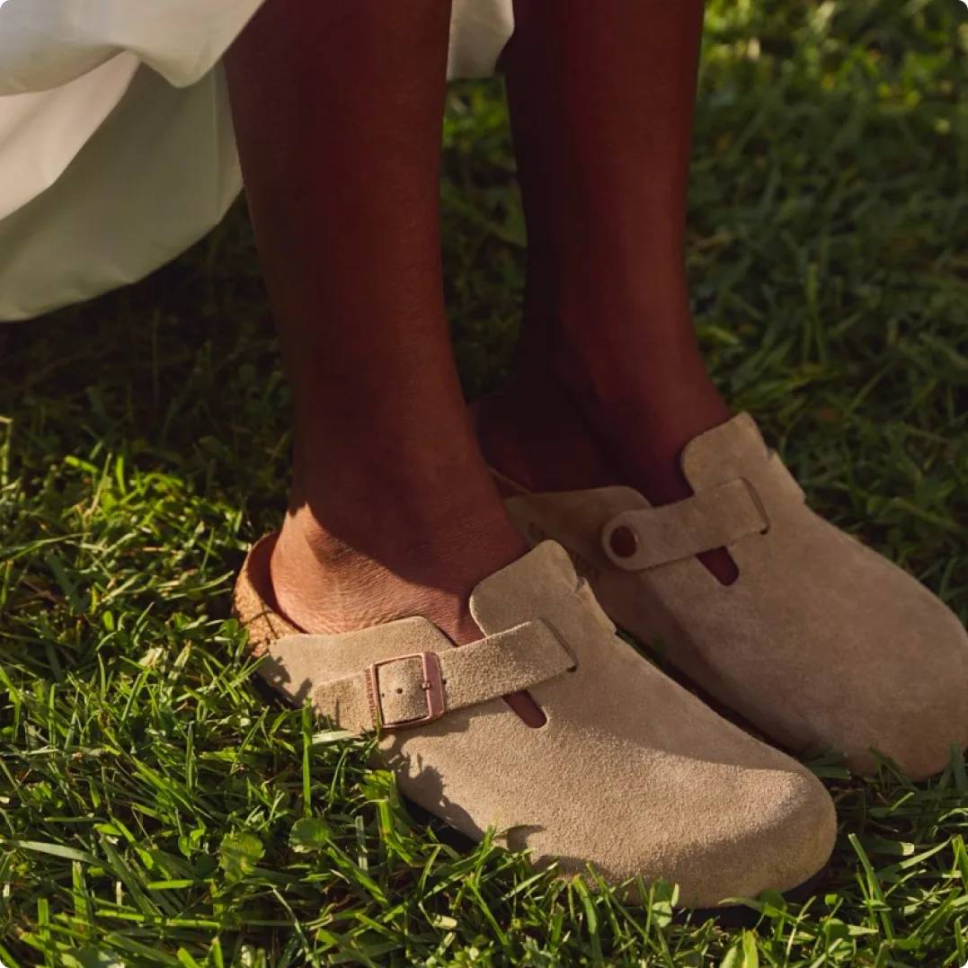 Person wearing light brown Birkenstock clogs in the grass