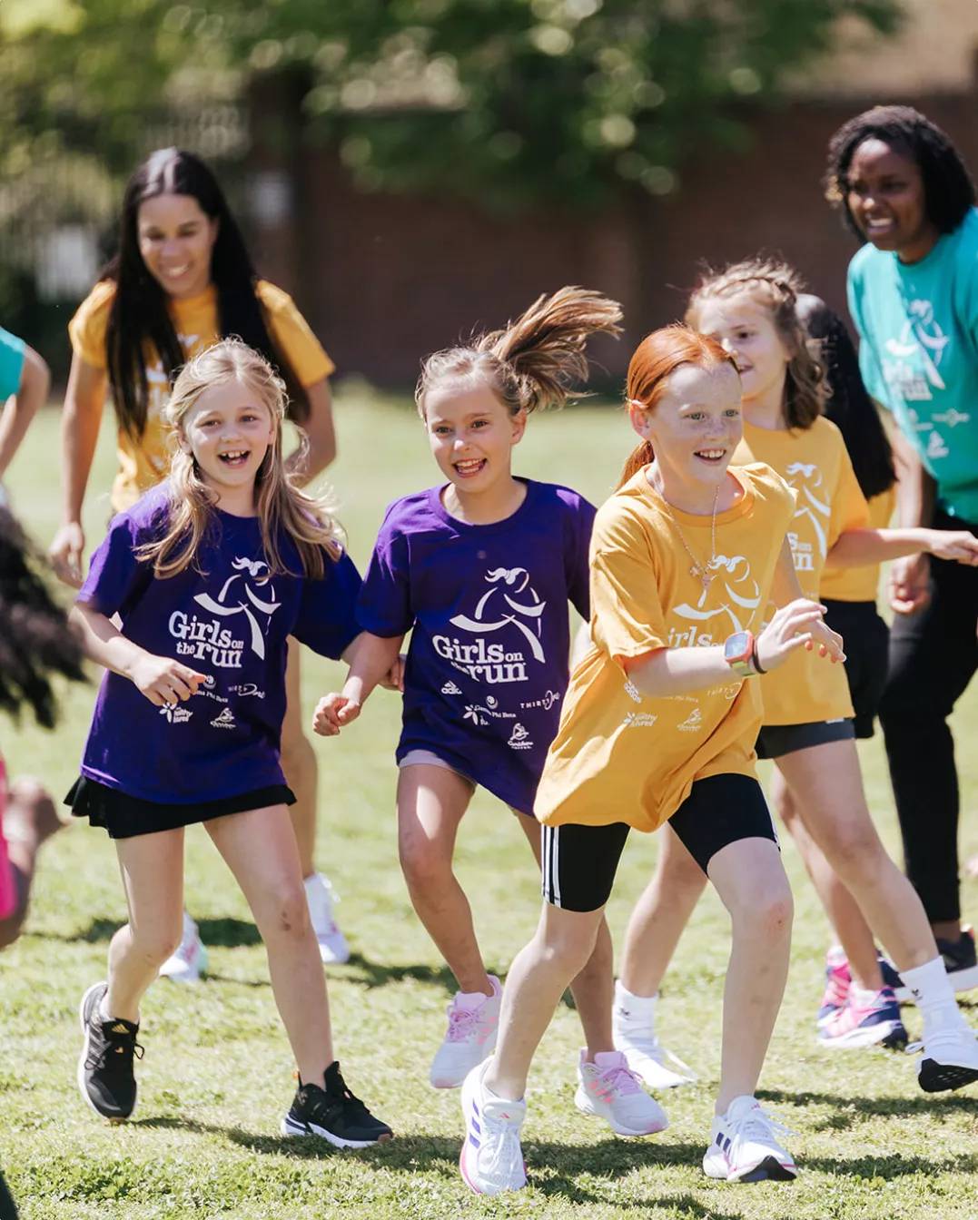 Young girls wearing yellow and purple t-shirts smiling and playing a game outside.
