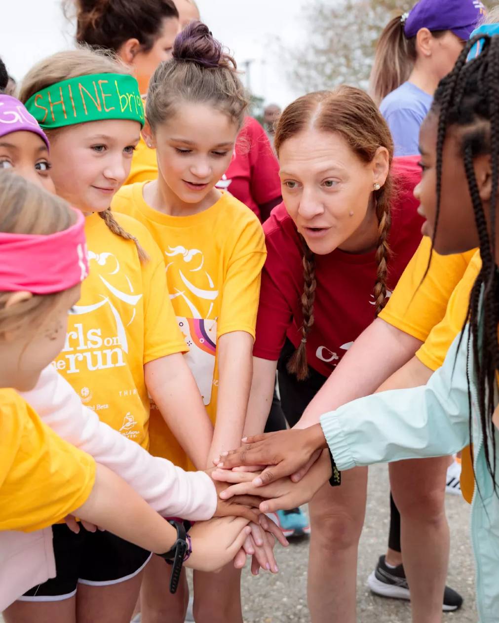 Featuring a team of six girls wearing matching yellow shirts huddled together with their hands in.