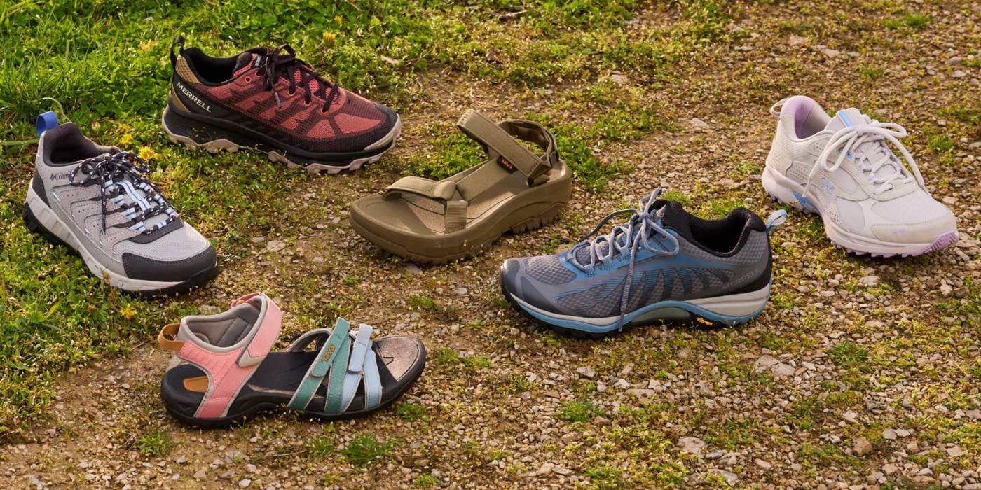 Various types of hiking shoes and sandals on outdoor terrain