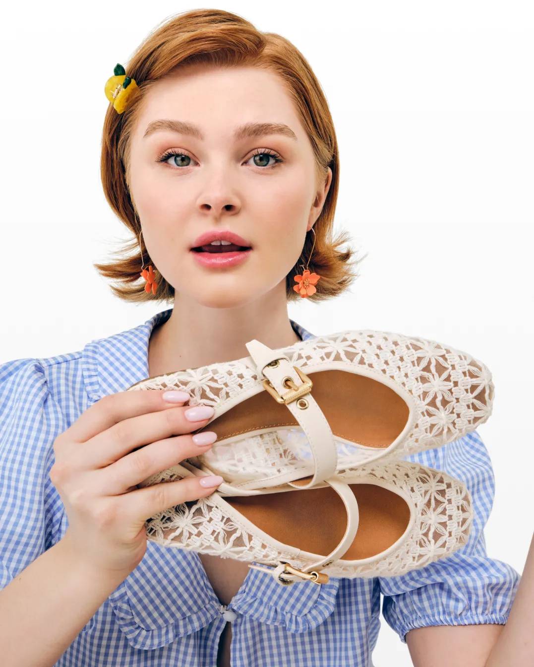 Featuring a model holding white ballet flats with lace detail and a gold buckle.