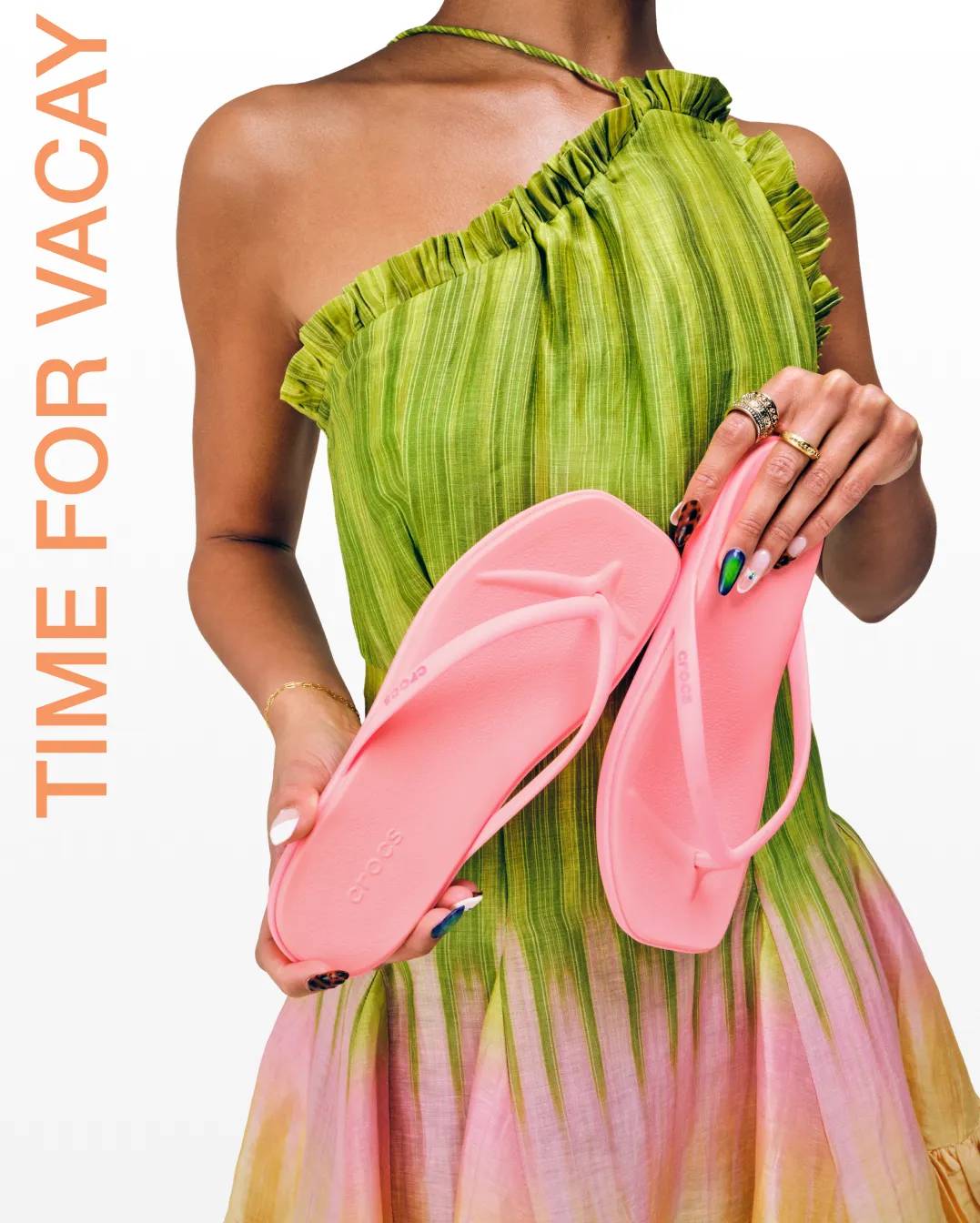 Featuring a woman in a lime green dress holding a pair of pink Crocs flip flops.